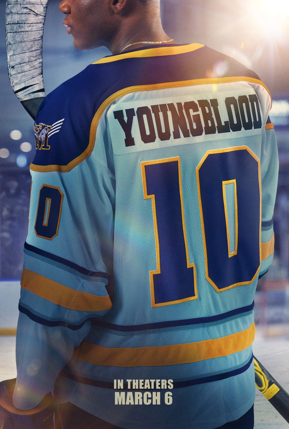 A poster for the film Youngblood shows a person standing on an ice hockey rink, viewed from behind. The person is wearing a blue, white, and yellow hockey jersey with the name “YOUNGBLOOD” printed across the upper back and the number 10 displayed in large block lettering below. A hockey stick is held upright beside the shoulder. The background features arena lights and a softly blurred crowd, creating a bright, icy atmosphere. At the bottom of the poster, bold white text reads “IN THEATERS MARCH 6.”